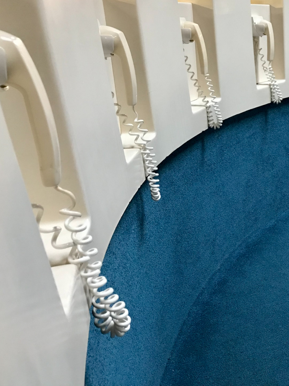Row of white corded phones with earpiece only on blue carpet